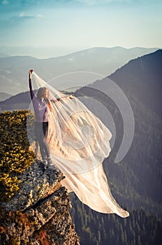 Girl with the light pink fabric playing with wind on mountains