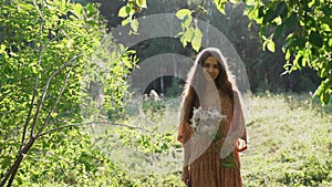 A girl in a light summer dress walks in a sunny forest. The girl looks at the camera and smiles. Summer mood. Candid portraits