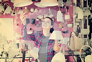 Girl in lighter shop choosing modern glass chandelier for house