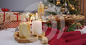 A girl lights golden and white candles at Christmas. On the New Year's table, gifts, a Christmas tree, decorations