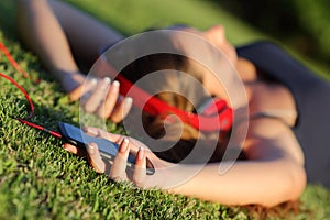 Girl listening music with headphones and holding a smart phone lying on the grass
