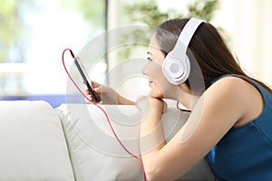 Girl listening music with headphones on phone on a couch
