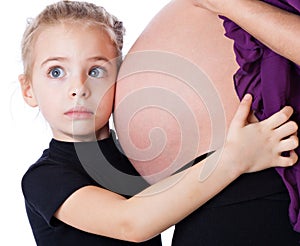 A girl is listening to the abdomen of her mother