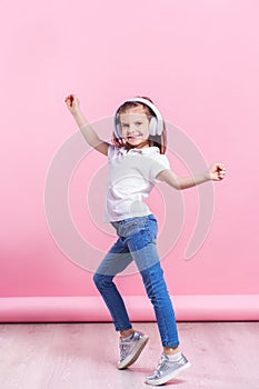 Girl listening to music in headphones an dance on pink background. Cute child enjoying happy dance music, close eye`s