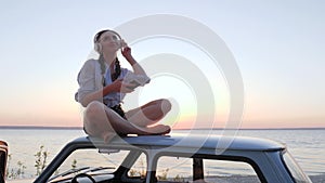 girl listening to music on headphones on roof classic car