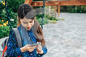Girl listening to music on her phone while sitting on a swing with a backpack behind her back