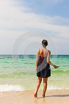 Girl listening to music on the shore facing the sea while holding smartphone