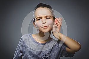 Girl listens. child hearing something, hand to ear gesture on grey background.