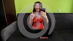 The girl listens to hard rock while sitting in a lotus position with a smartphone in her hands and headphones on her head.