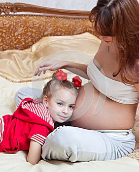 A girl listens to the mother's abdomen