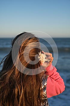 a girl listens to a seashell on the beach