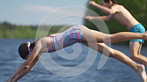 Girl and little boy in wetsuit jumping into the lake from wooden pier. Having fun on summer day.