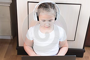 Girl Little child in headphones uses a laptop intently while sitting on the floor in her room