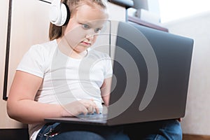 Girl Little child in headphones uses a laptop intently while sitting on the floor in her room