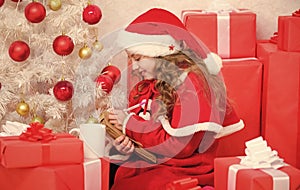 Girl little cute child hold pen and paper near christmas tree. Wish list. Letter for santa. Kid santa hat enjoy