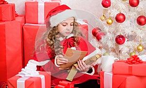 Girl little kid hold pen and paper near christmas tree writing letter. Child write letter to santa claus. Child santa