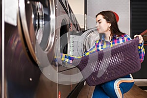 Girl loads laundry into a washing machine. woman in public laundry