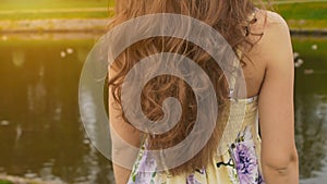 A girl with long, beautiful and curly hair against the backdrop of a pond in the park. Hair close-up. The girl sensually