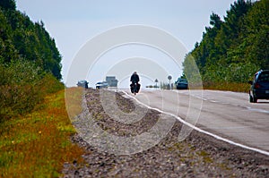 A girl on a long bike journey rides along the side of an asphalt road.