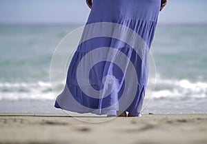 The girl in a long blue skirt stands on the bank of the sea