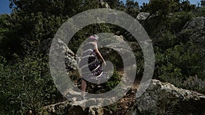 A girl in a long dress climbs a stone rock on a sunny day