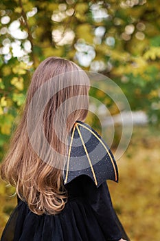 Girl with long hair in bat costume for Halloween. Back view.