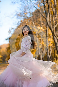 girl with long hair in a beautiful light puffy dress is spinning on the alley in the park