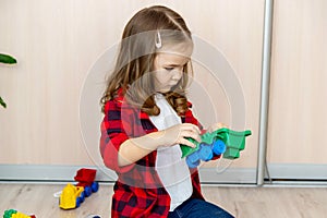 A girl with long hair builds from a plastic construction kit. The girl plays at home