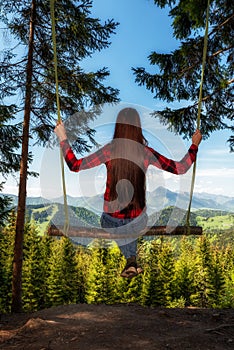 Girl with long hair on forest swing with beautiful mountain view