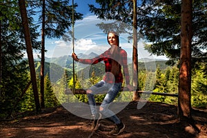 Girl with long hair on forest swing with beautiful mountain view