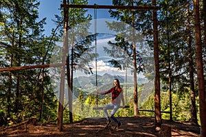 Girl with long hair on forest swing with beautiful mountain view