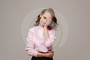 A girl with long hair on a gray background suffering from a headache holds her head with her hands. The girl puts her hands on her