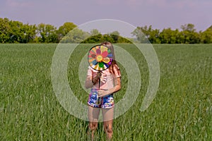 A girl with long hair holds in her hands a colored windmill toy on a green field on a sunny day