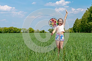 A girl with long hair holds in her hands a colored windmill toy on a green field on a sunny day