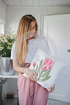 a girl with long hair holds a pillow with a painted tulip