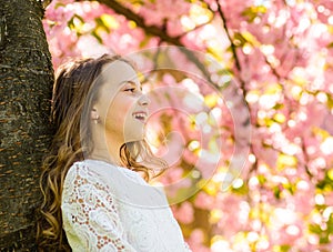 Girl with long hair outdoor, cherry blossom or sakura on background. Cute child enjoy nature on spring day. Unite with