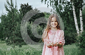 Girl with long hair in a pink dress smiles against a background of greenery