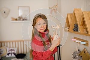 Girl with long hair in pink sweater in children`s room of  youngest child in family, climbed to wall shelves with toys and