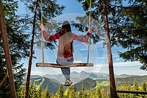 Dievča s dlhými vlasmi sa hojdá na lesnej hojdačke s krásnym výhľadom na hory