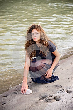 Girl with long wavy brown hair. With a stone in his hands along the bank of a river.