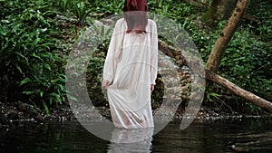 A girl in a long white dress goes into the water. Celebrating Ivan Kupala Day