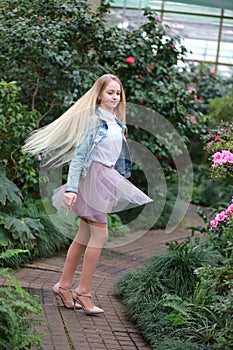 Girl with long white hair in a denim jacket walks in the garden with blooming azalea