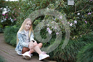 Girl with long white hair in a denim jacket walks in the garden with blooming azalea