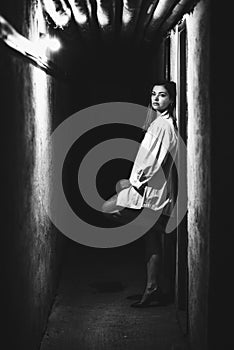 Girl in long white shirt with depressive expresion in dark hallway