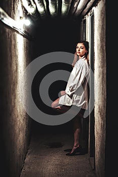 Girl in long white shirt with depressive expresion in dark hallway