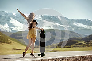 Girl with longboard is standing at mountain road