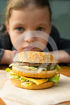 Girl looking at a big tasty burger from far away, front view