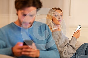 Girl Looking At Boyfriend Texting On Phone Suspecting Infidelity, Indoor photo