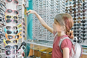 Girl looking and choosing sunglasses, child near shop window in eyewear store