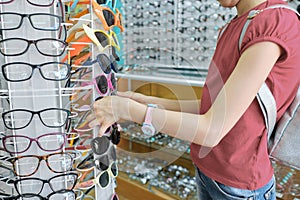 Girl looking and choosing sunglasses, child near shop window in eyewear store